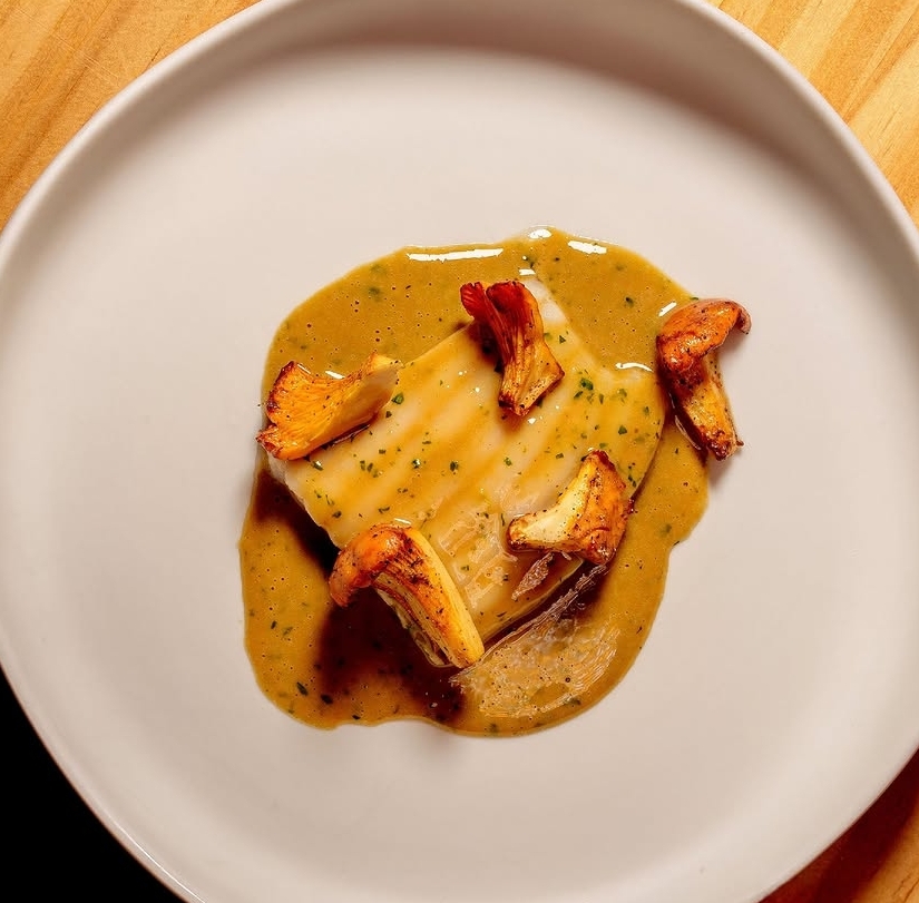 Cod fillet with chanterelles in a herb velouté on a white plate