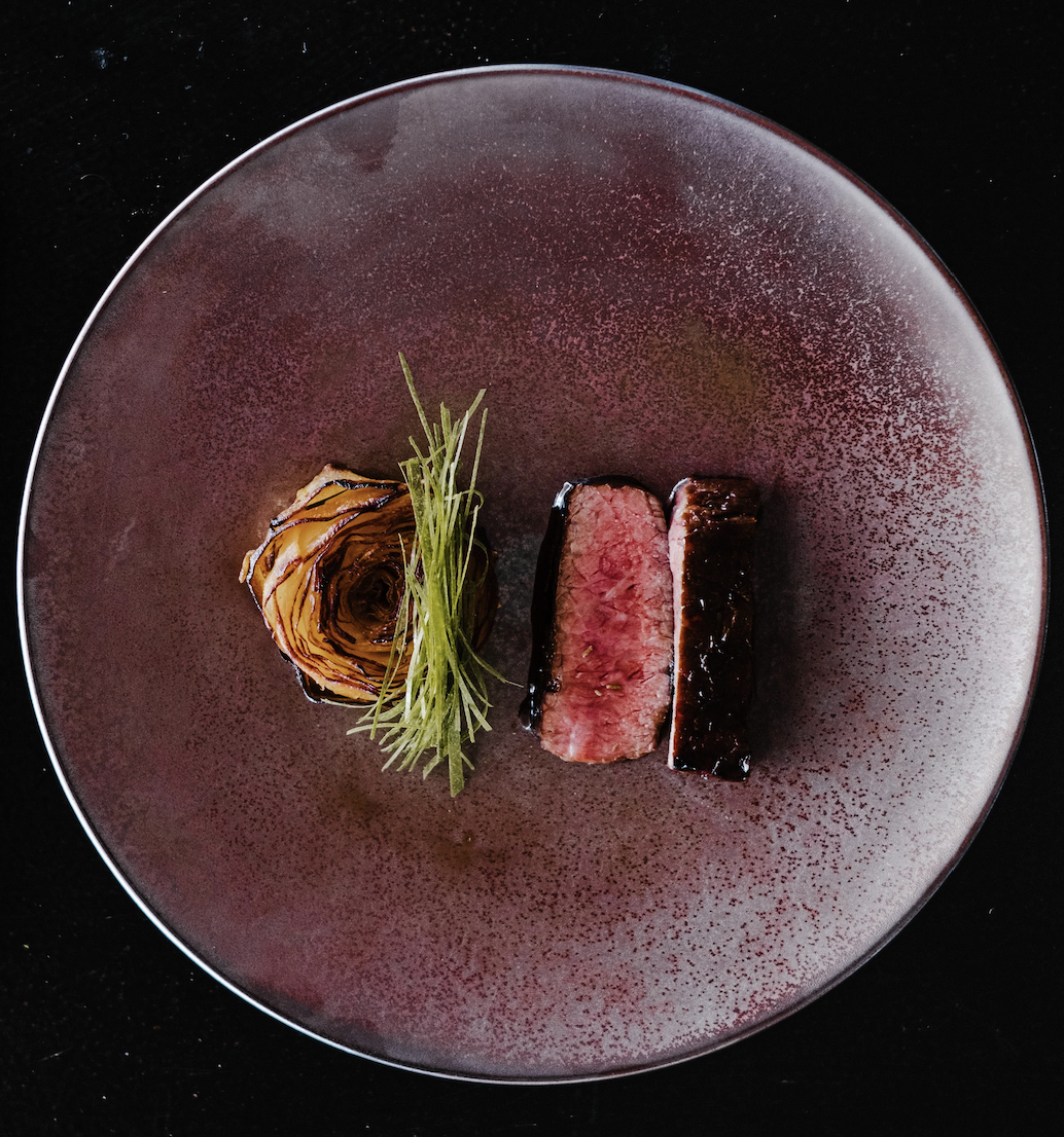 Glazed beef with charred artichoke on a burgundy speckled plate
