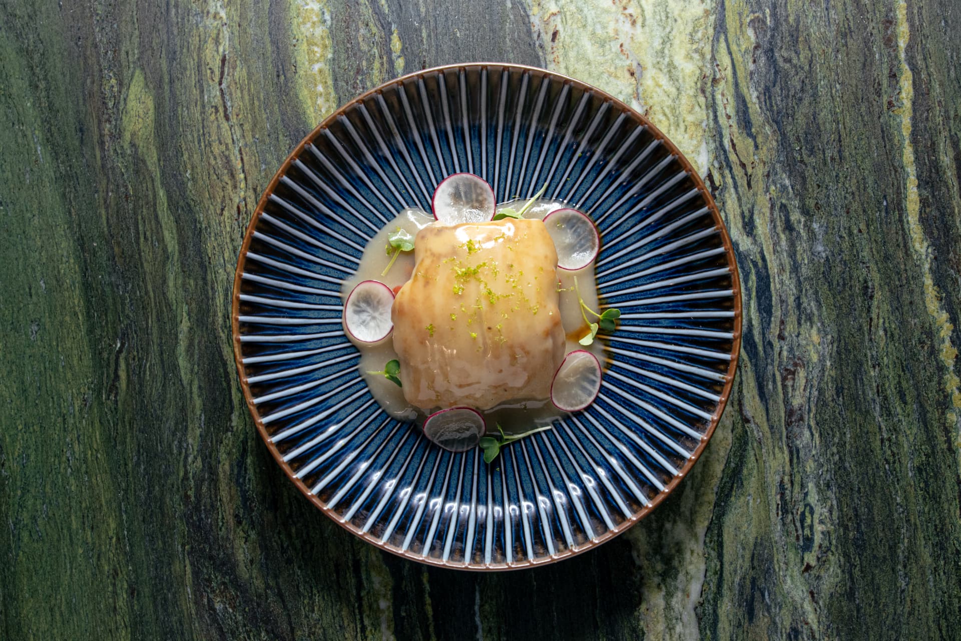 Glazed cod with radish on a blue ribbed plate over green stone