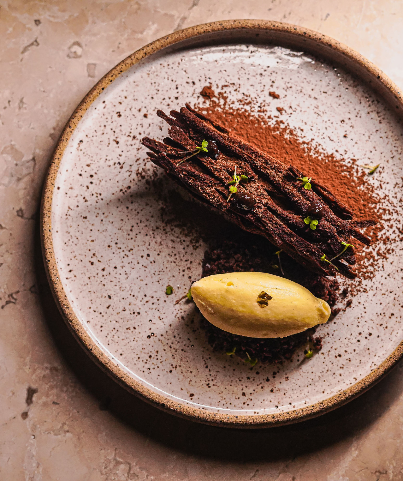 Chocolate mille-feuille with cocoa dust and mango quenelle on a speckled plate
