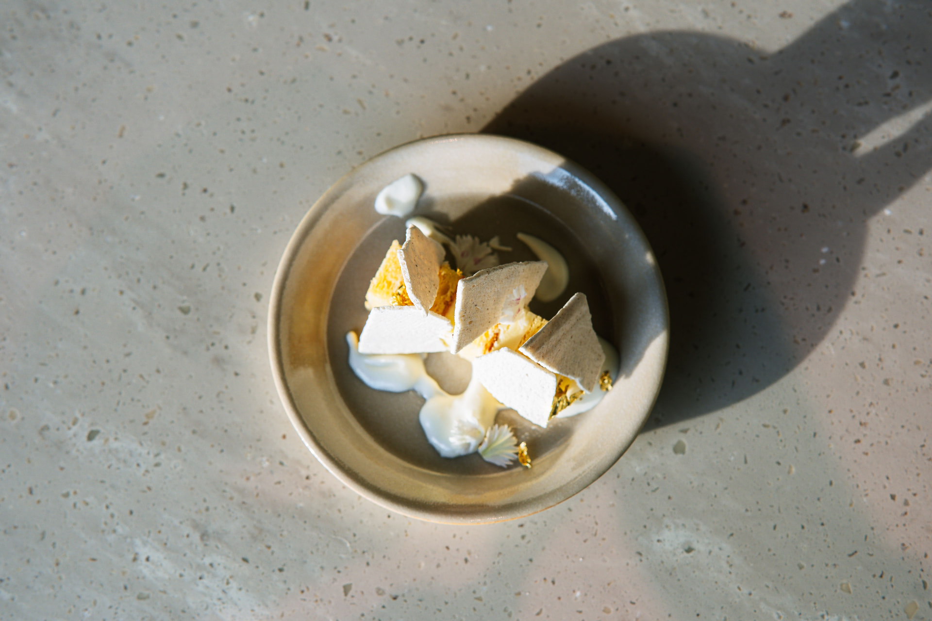 Meringue shards with cream and gold leaf in a sunlit ceramic bowl