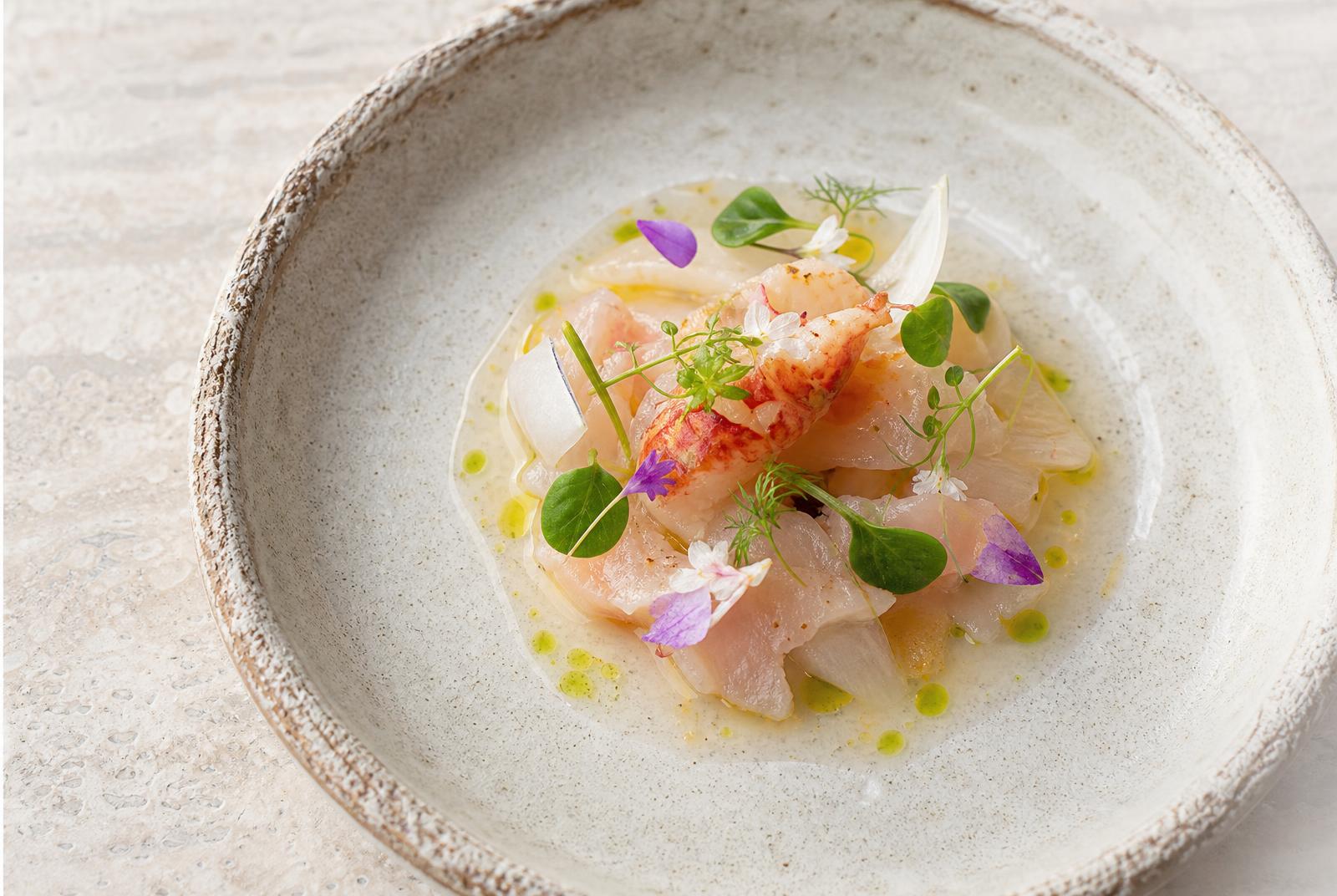Seared fish fillet with yellow sauce, vegetables and edible flowers in dramatic light