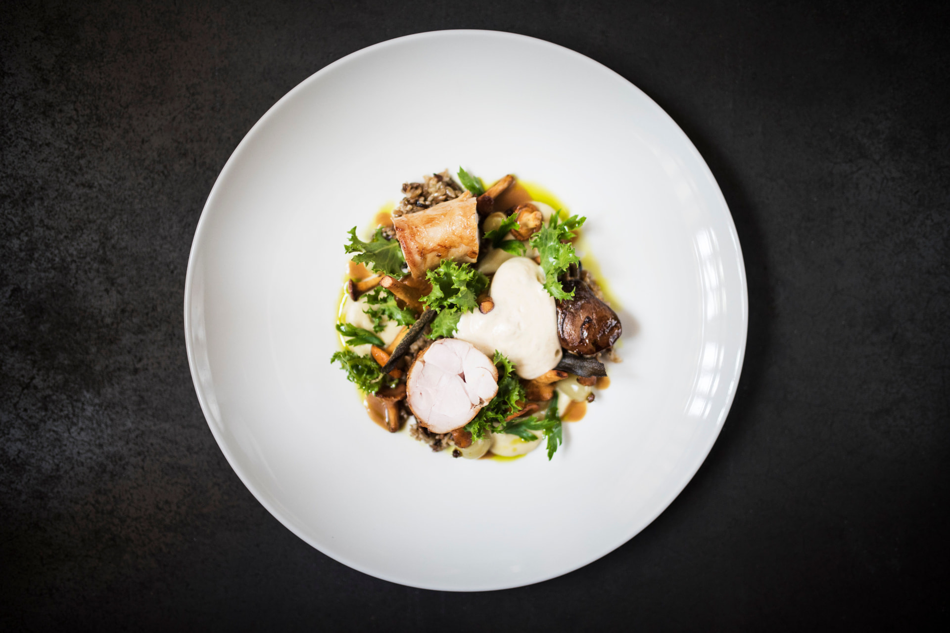 Poached poultry with chanterelles, wild rice and cream foam on a white plate