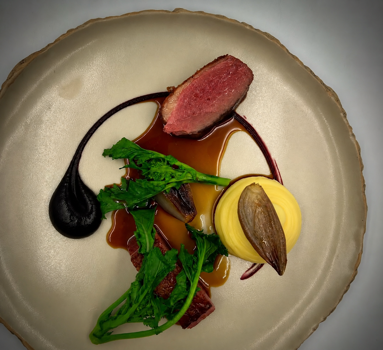 Seared beef with silky jus, potato purée and glazed vegetables on a ceramic plate