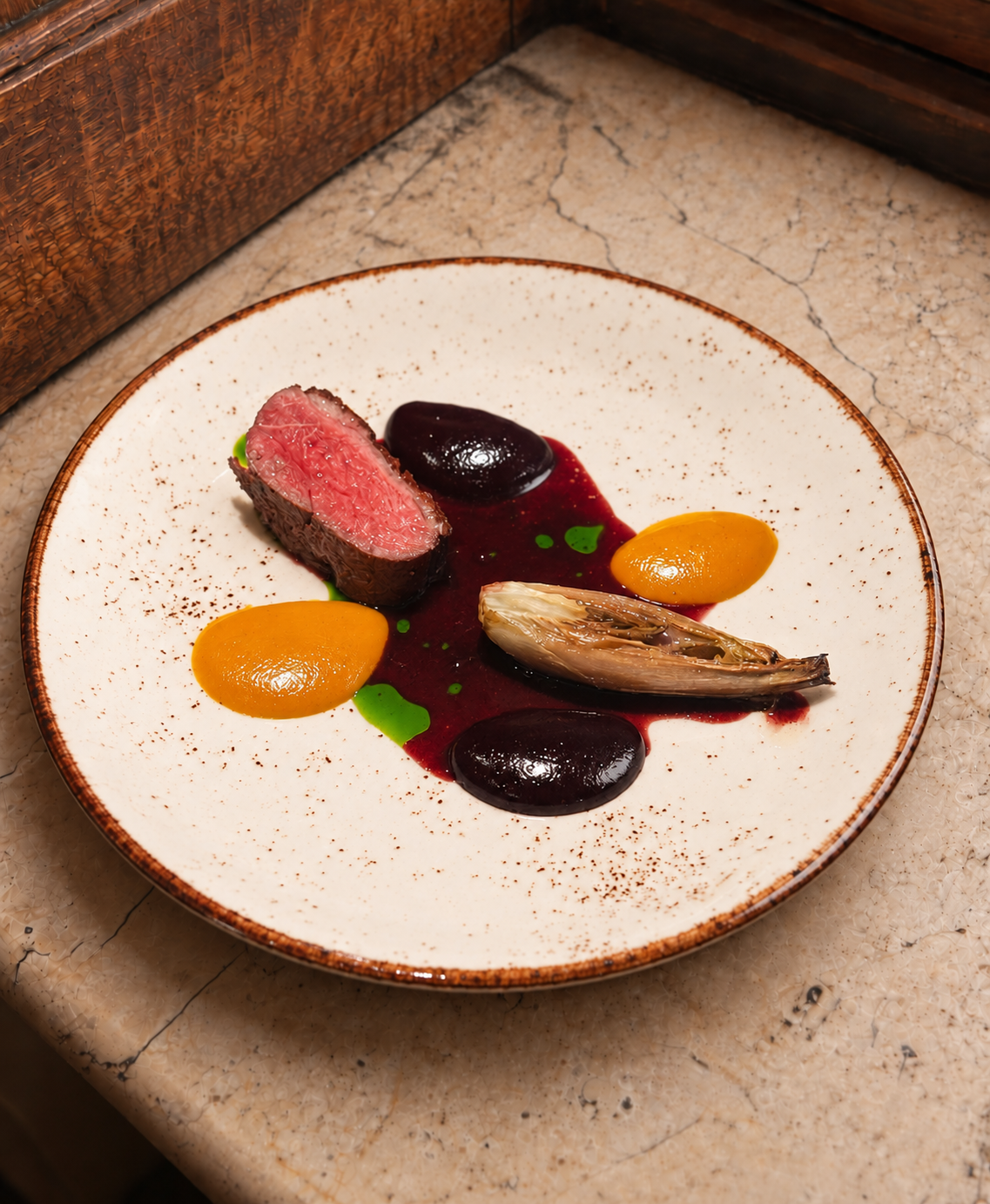 Sliced beef with beetroot, orange purée and endive on a ceramic plate