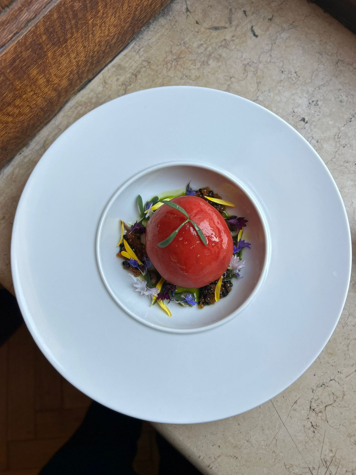 Tomato confit with caviar and edible flowers on a white plate