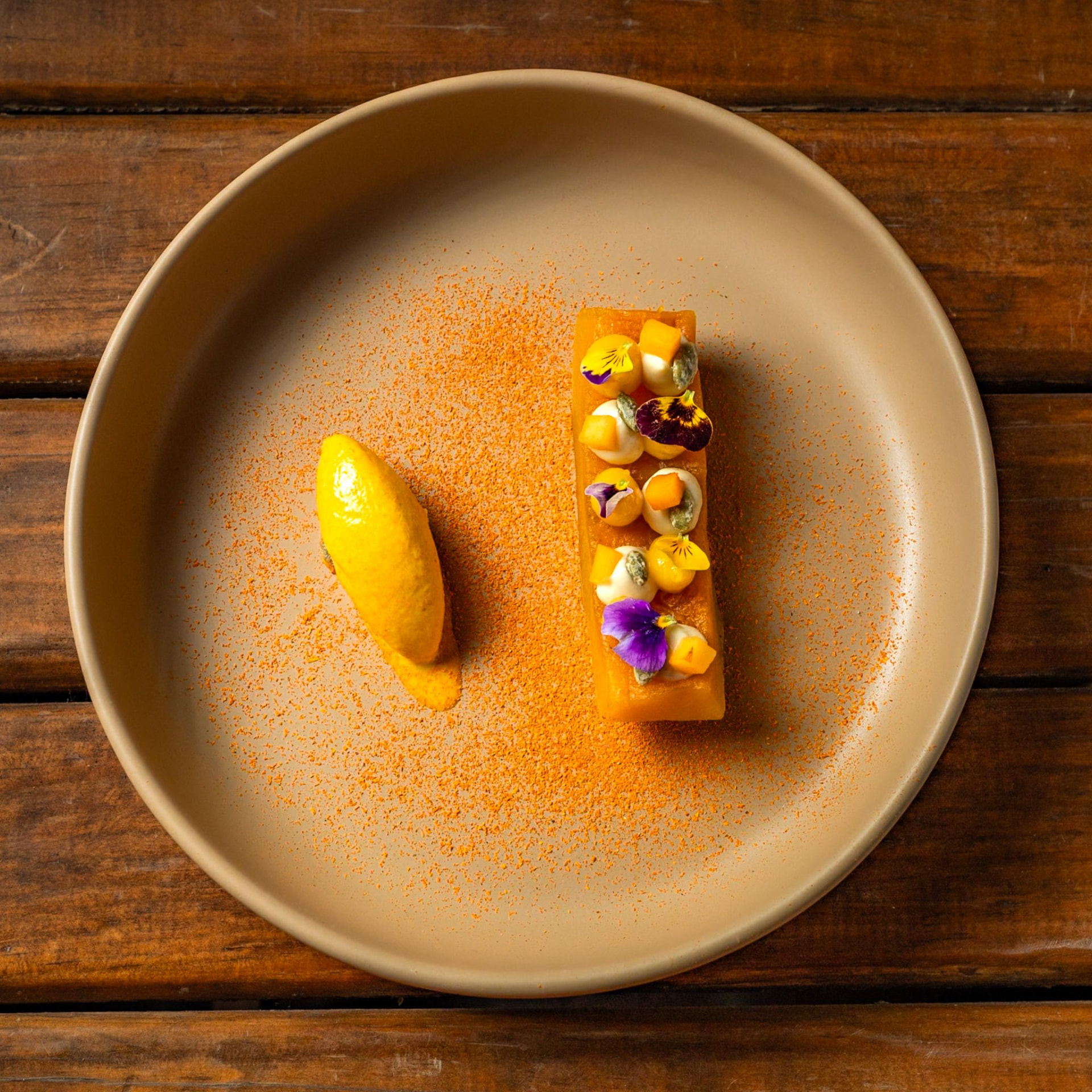 Pumpkin terrine with edible flowers and citrus quenelle on a sand ceramic plate