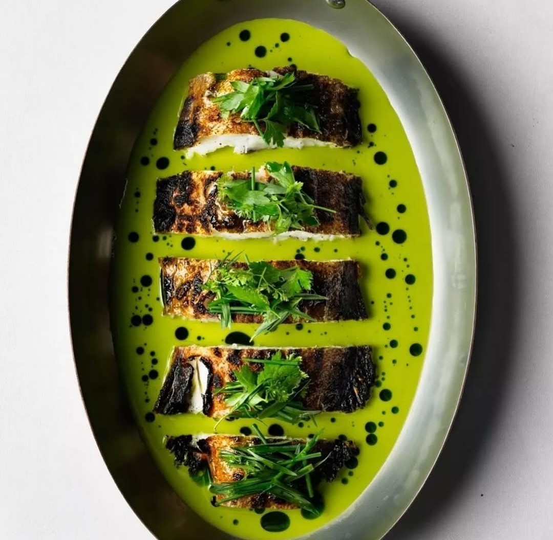 Charred fish fillets in a vivid green herb sauce on a silver platter